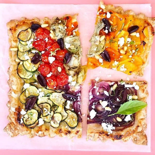A square vegetable tart with zucchini, artichokes, tomatoes, bell peppers, and Follow Your Heart Feta Crumbles, cut into quarters.