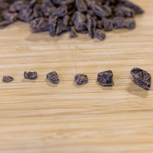 A line of different sized TCHO Dark Chocolate Chunks, from a small pebble shape on the left to a small rock shape on the right.